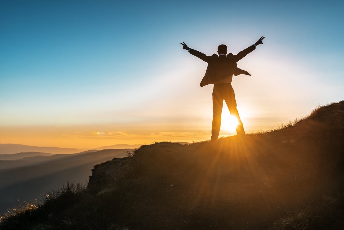 Silhouette of Businessman on Top of the Mountain at Sunset